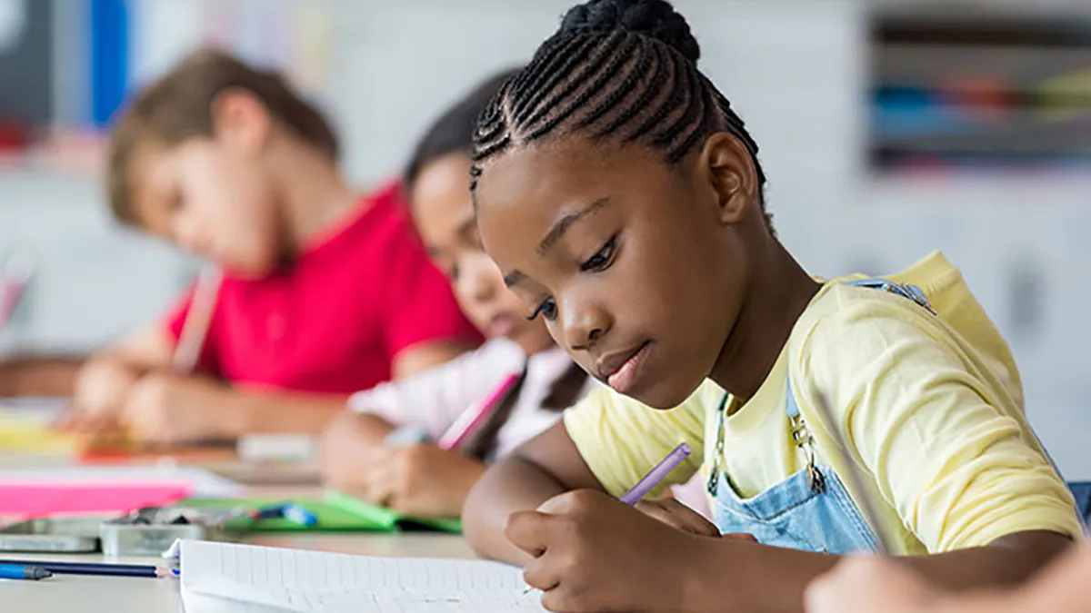 Young students sit writing at their desks.